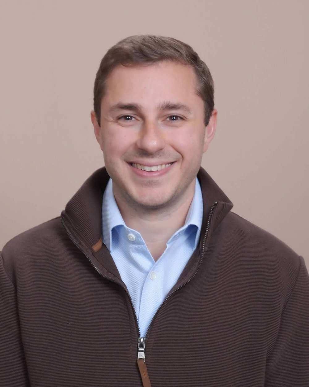 Portrait of Dr. Gregory Inzinna, smiling, in a brown quarter-zip sweater over a light blue shirt